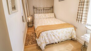 Et soveværelse med seng, et sengebord med lampe, et spejl, et billede på væggen og et vindue med gardiner.