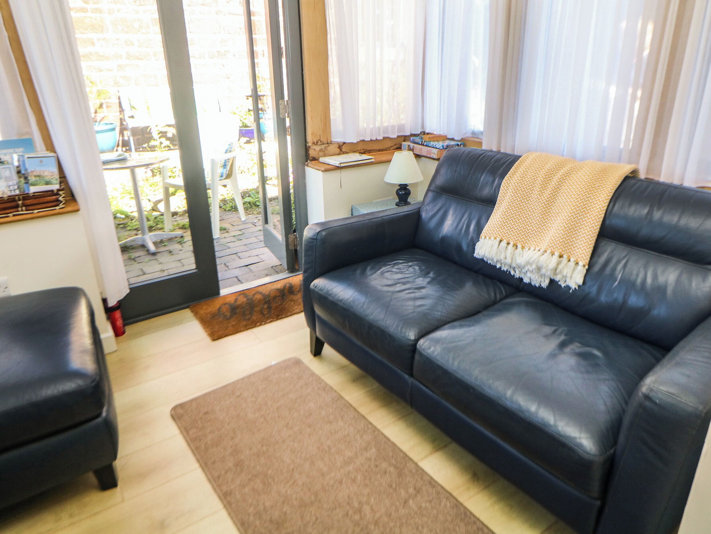 Uma sala de estar com sofá de couro preto, tapete marrom e mesa lateral de madeira com luminária.