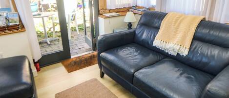 En stue med en sort lædersofa, en brun måtte og et træsidebord med en lampe.