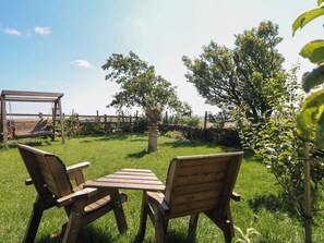 A wooden bench and table set in a grassy outdoor area with a stone structure and trees in the background. - The Netty (Buxton)