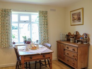Un comedor con mesa de madera, sillas y una ventana con cortinas florales.