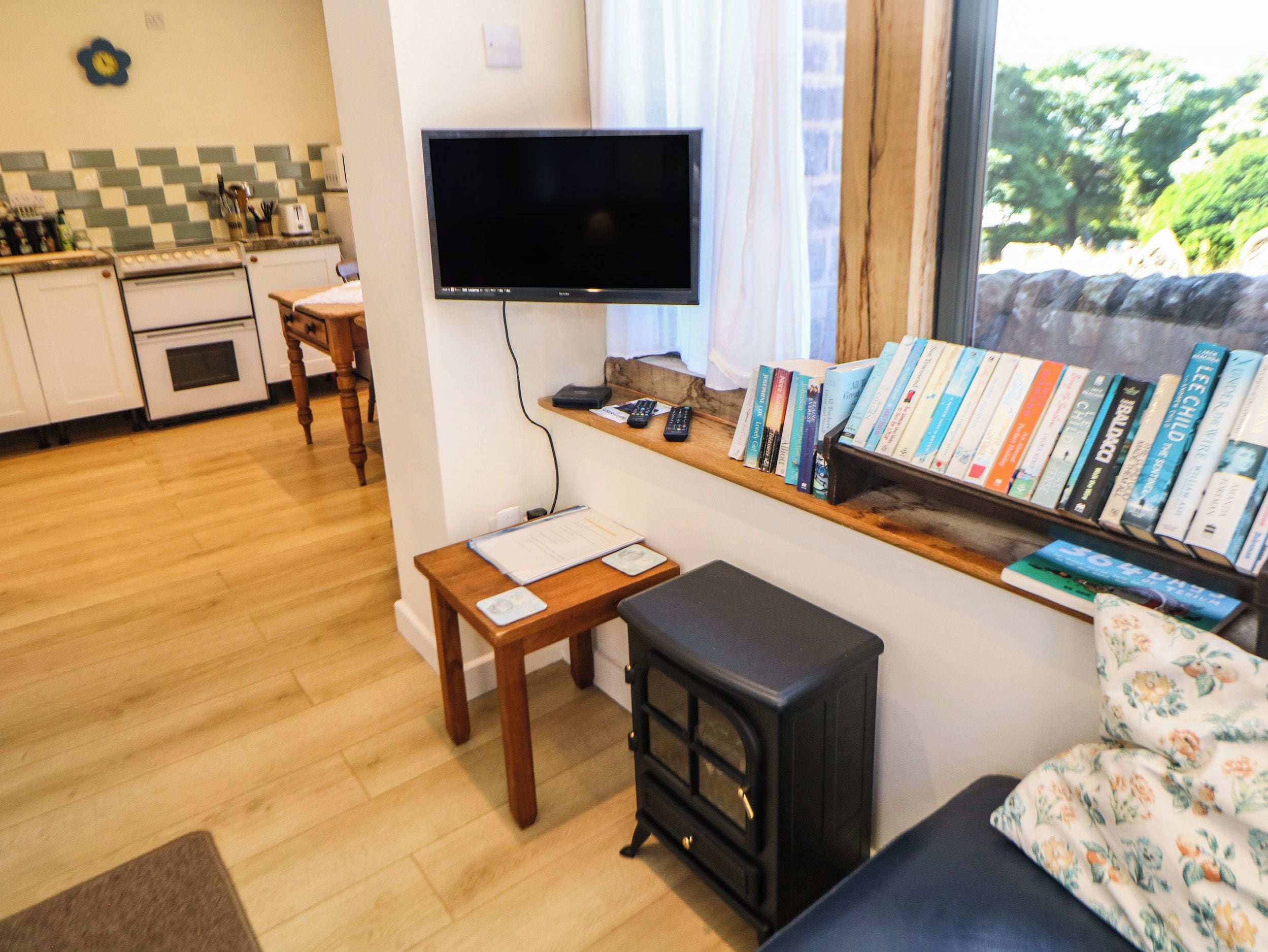 A cozy living area with a flat-screen TV, a small table, a sofa, a bookshelf with books, and a wood-burning stove.