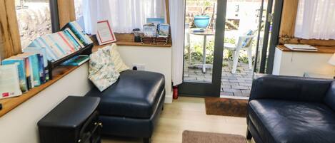 A room with a black leather sofa, a black ottoman, a wooden table with books, and a window with curtains.