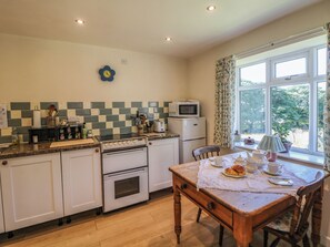 A kitchen with a dining table set for two, a microwave, and a refrigerator. - The Netty (Buxton)