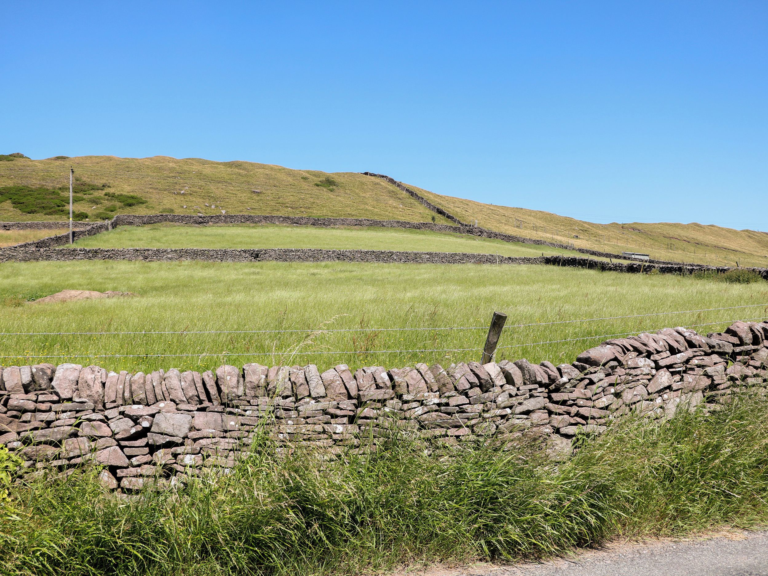 A stone wall with a grassy field and a clear blue sky.