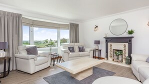 Ein modernes Wohnzimmer mit Kamin, zwei Sofas, einem Couchtisch und Blick ins Grüne.