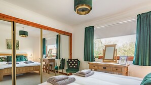 Ein Schlafzimmer mit einem großen Bett, einem Schreibtisch, einem Stuhl, einer Kommode, einem Spiegel und einem Fenster mit Vorhängen.