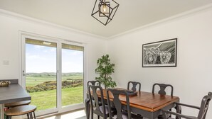 Ein Essbereich mit Holztisch und -stühlen, Blick auf einen Golfplatz durch eine Schiebetür und ein gerahmtes Bild an der Wand.