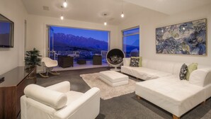 Una sala de estar moderna con un sofá blanco, un sillón blanco y una silla redonda. Se aprecia una ventana grande con vistas a la montaña.