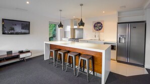 Una cocina moderna con una isla central, taburetes de bar, un refrigerador de acero inoxidable y un televisor de pantalla plana montado en la pared.