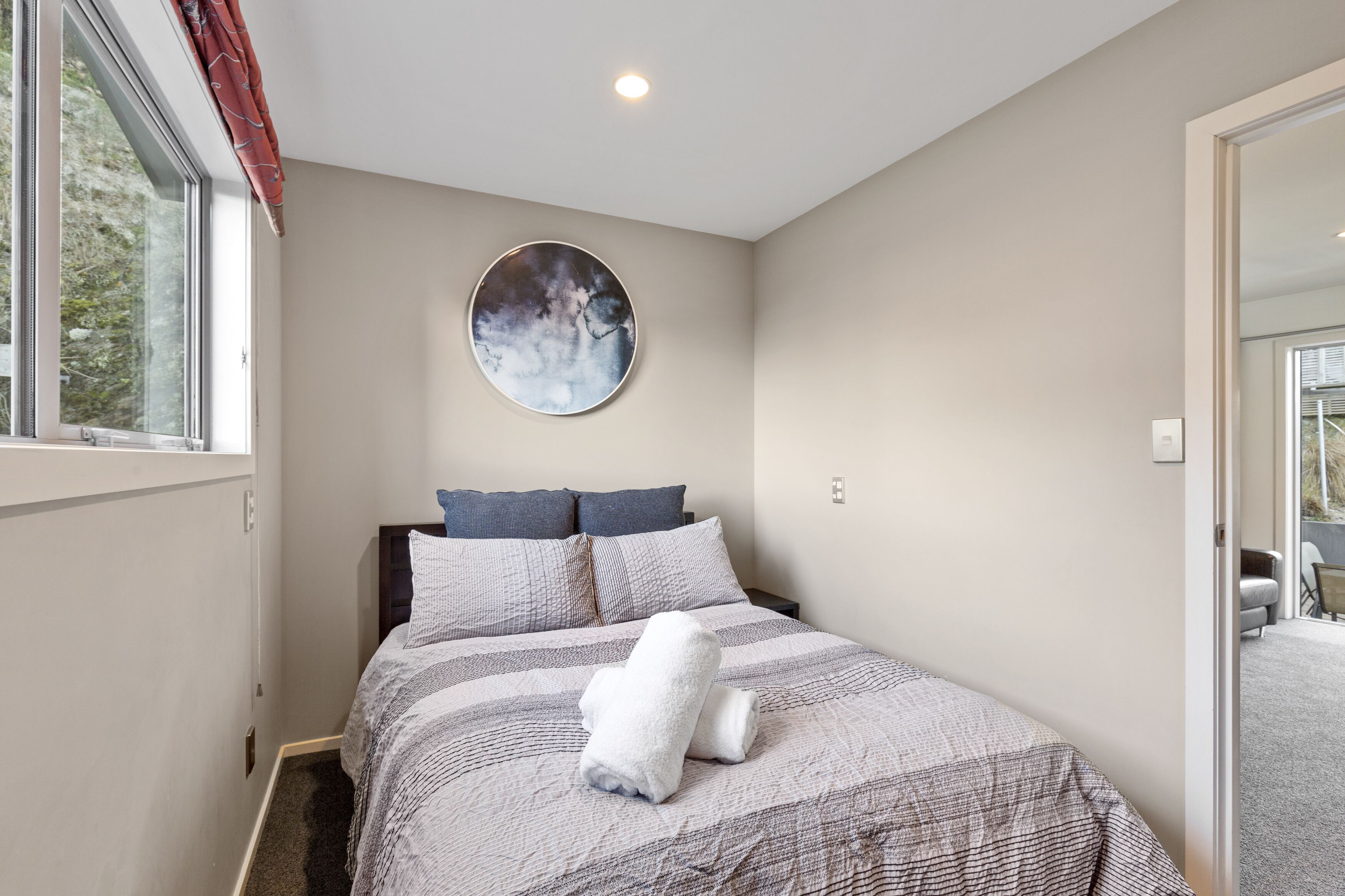 A bedroom with a bed, a round mirror, and a window with curtains.