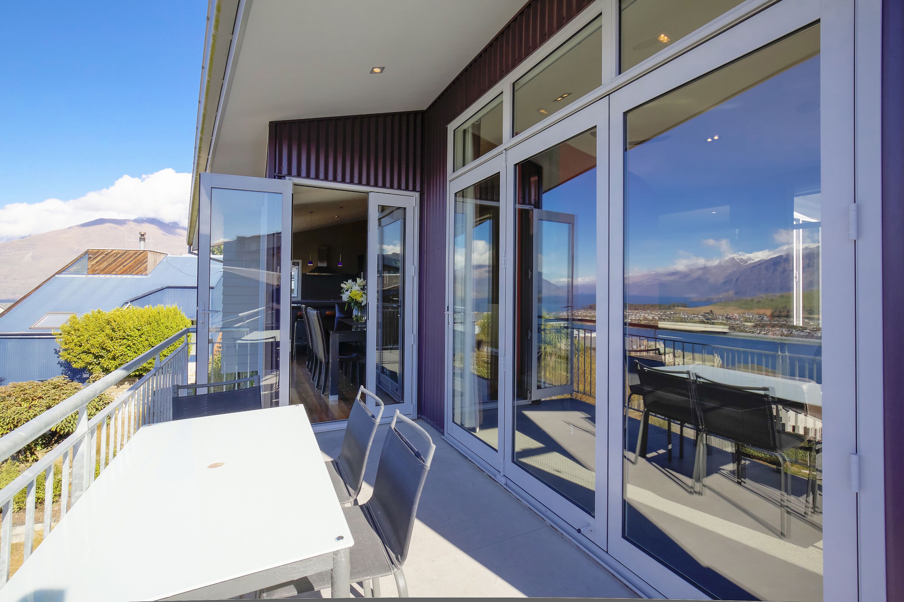 A balcony with a table and chairs, large glass doors, and a view of mountains and a body of water.