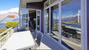 A balcony with a table and chairs, large glass doors, and a view of mountains and a body of water.