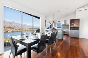 A modern kitchen with a large island, a dining area with a view of a lake and mountains, and a spacious living area. - Paradise Peaks - Queenstown Holiday Home (Queenstown)