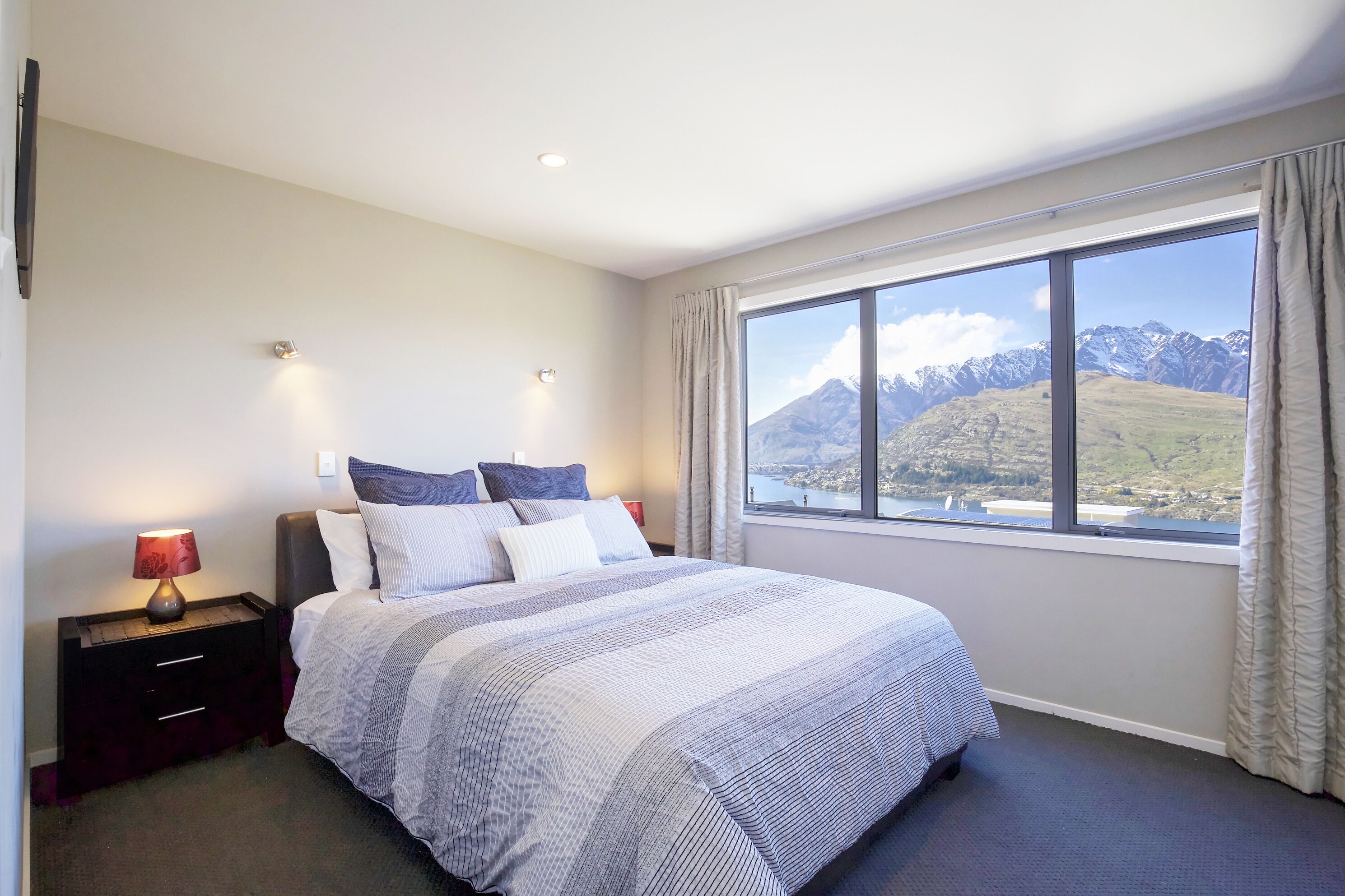 Een slaapkamer met een groot bed, een nachtkastje met een lamp en een raam met uitzicht op bergen.