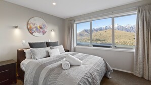 A bedroom with a large bed, a view of mountains, and a painting on the wall.