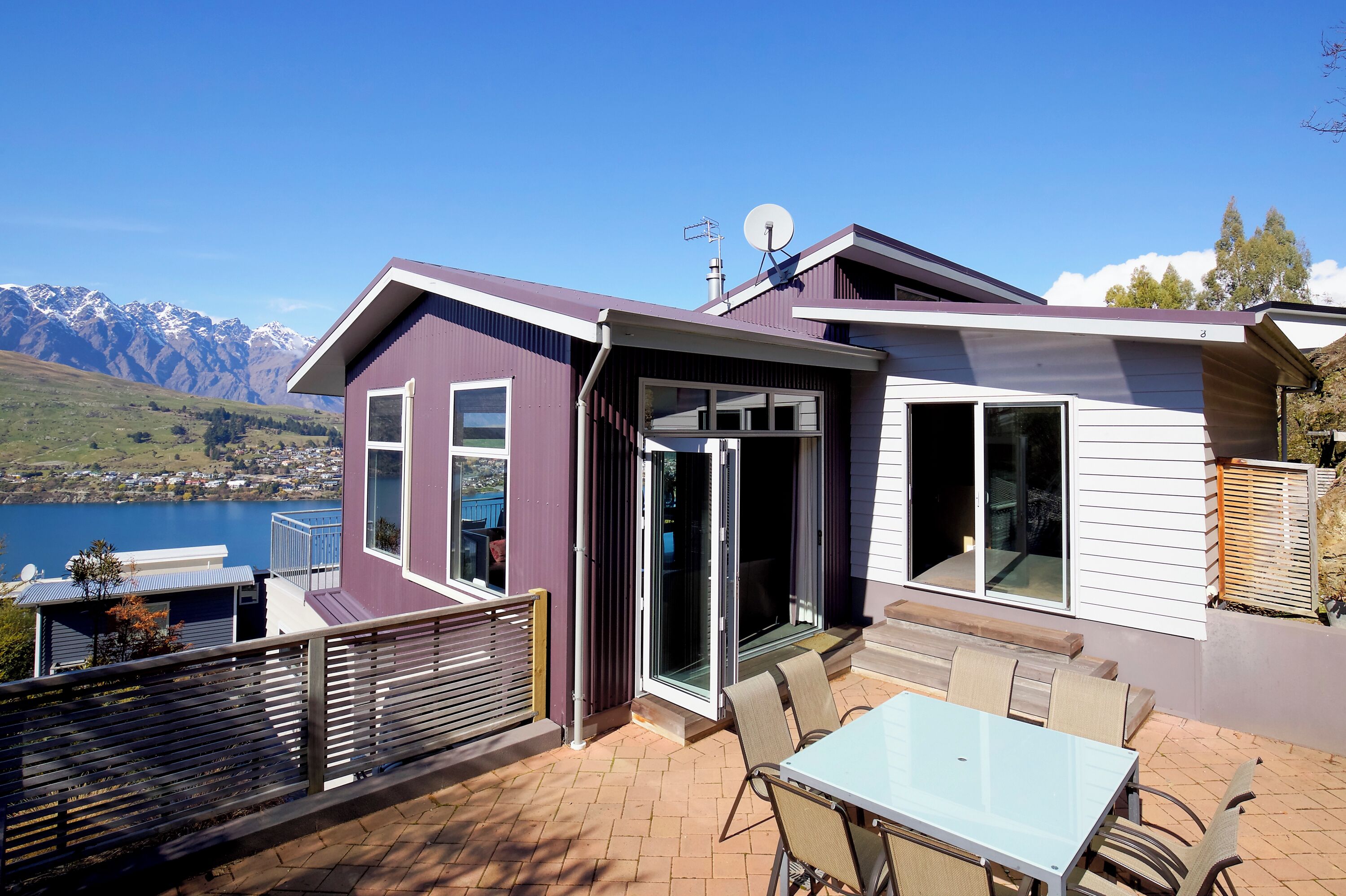 A modern house with a patio, large windows, and a view of mountains and a lake.
