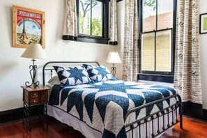 Een bed met een blauw-witte quilt, twee bedlampen, een houten nachtkastje en een poster aan de muur.