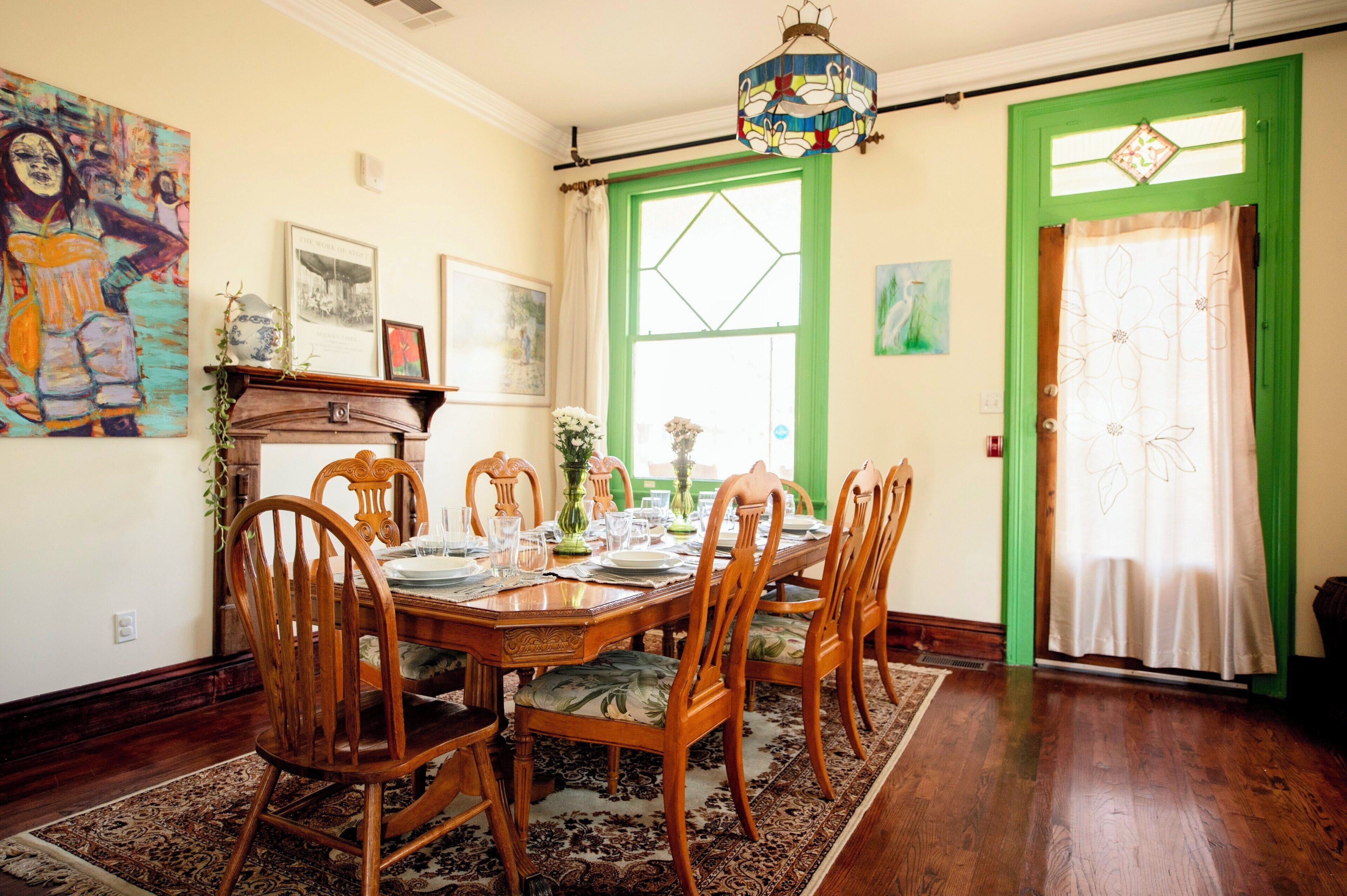 A dining room with a wooden table set for four, surrounded by chairs, a green door, and a stained glass light fixture.