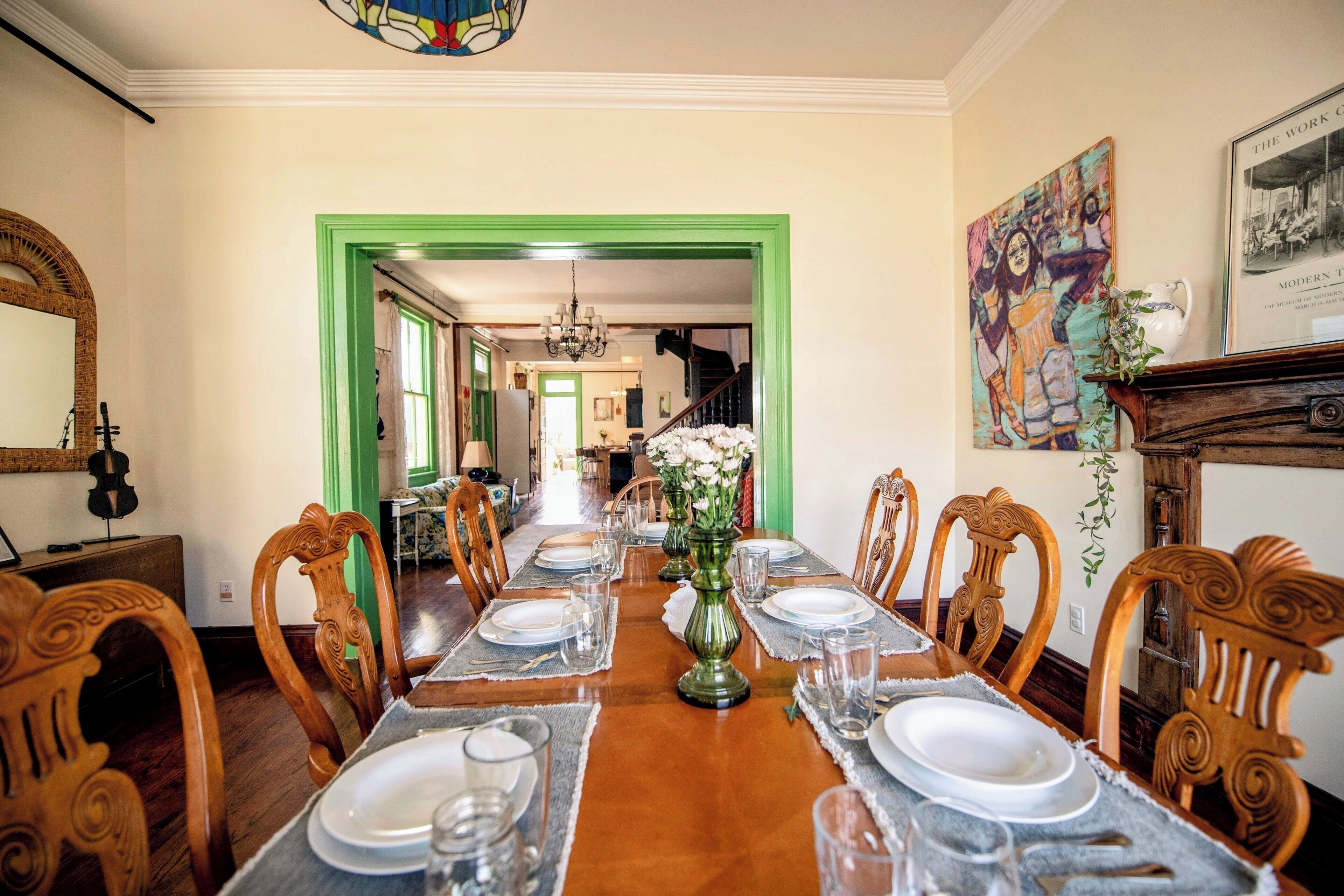 A dining room with a long table set for six, flanked by wooden chairs with intricate carvings.