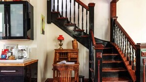 Un escalier avec des balustrades en bois et une rampe noire, un bureau en bois avec une lampe rouge et un meuble avec une porte en verre dépoli.