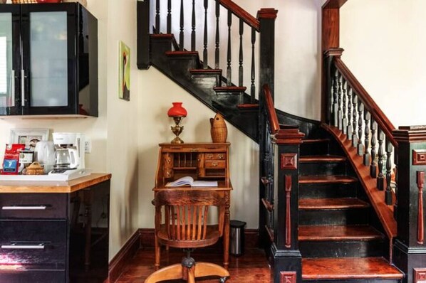 Una escalera con barandillas de madera y un pasamanos negro, un escritorio de madera con una lámpara roja y un armario con puerta de vidrio esmerilado.