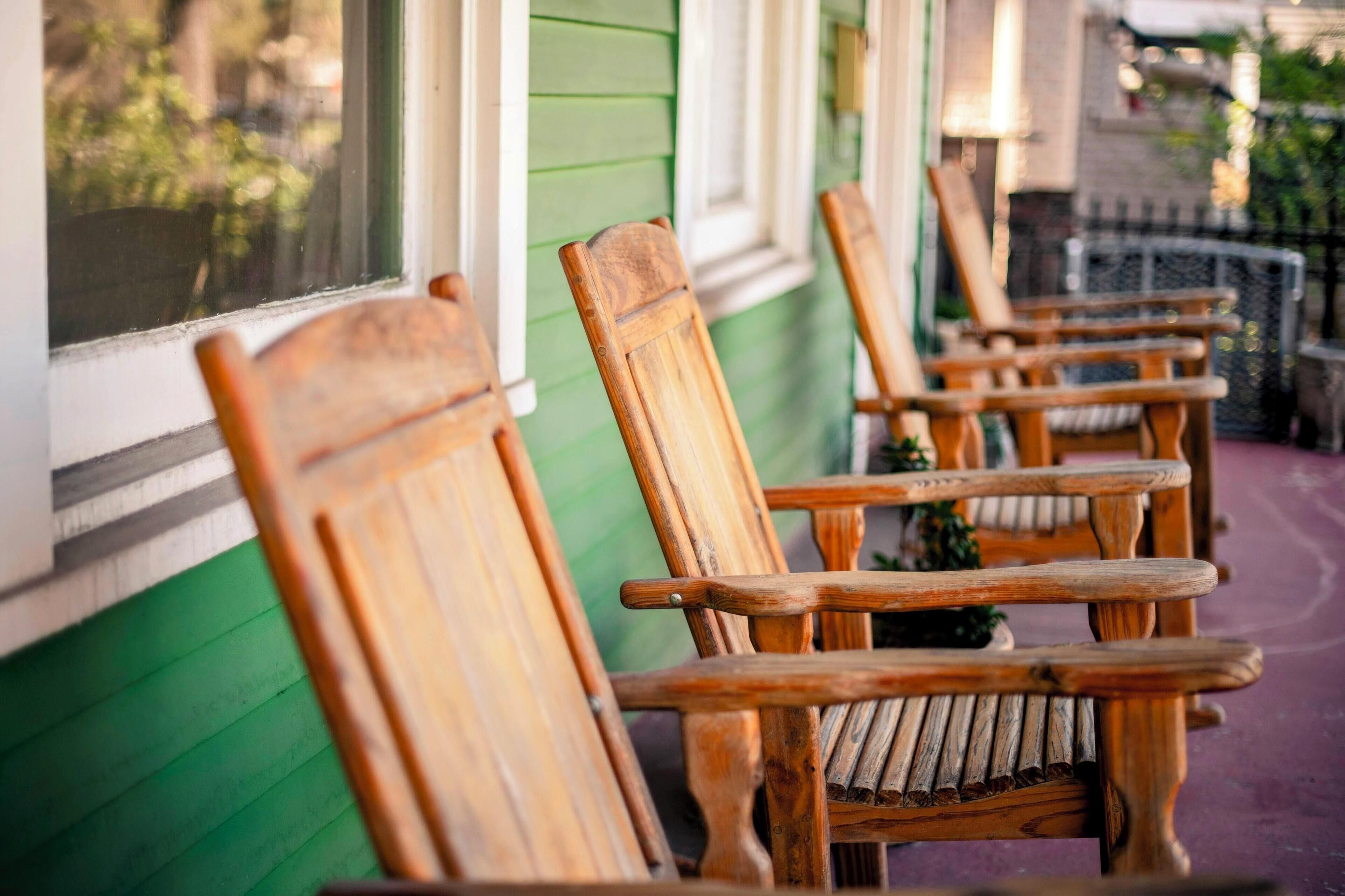 En række træ Adirondack-stole på en veranda med grønt panel og et vindue.