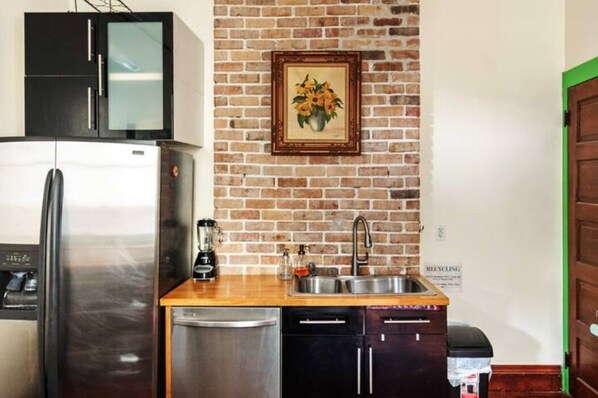 Een compacte keuken met een bakstenen muur, roestvrijstalen apparatuur en een ingelijste kunstwerk.