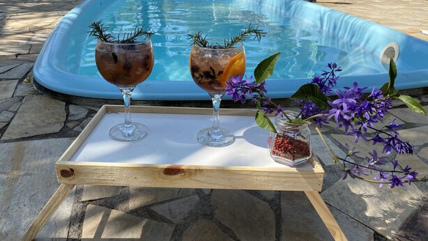 A poolside setting with two glasses of a beverage on a wooden tray, surrounded by a pool and outdoor furniture. - Recanto das Orquideas II (Quatis)