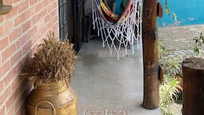 A covered porch with a hammock, a potted plant, and a door leading to a room. - Recanto das Orquideas II (Quatis)