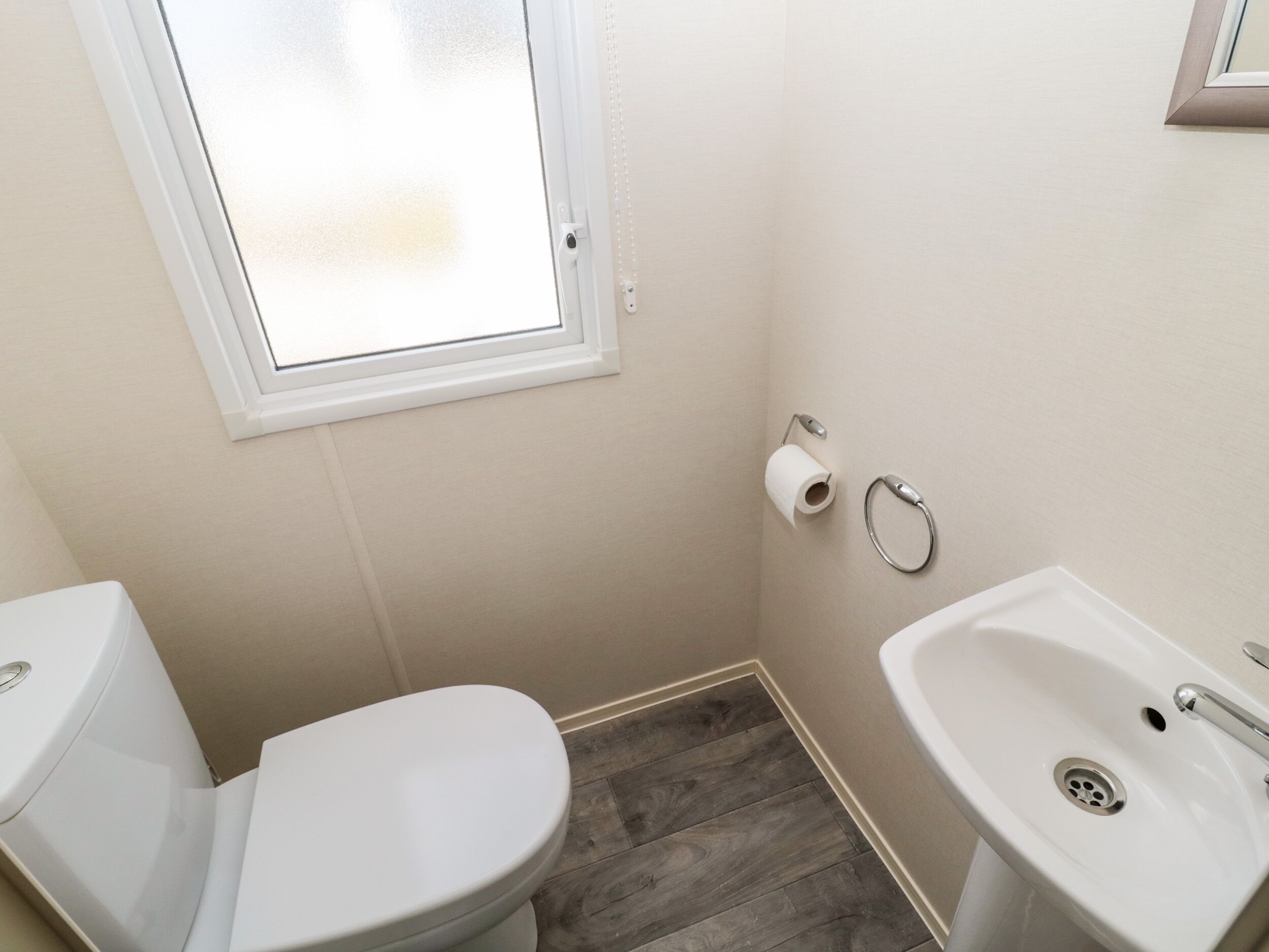 A small bathroom with a toilet, a sink, and a window.