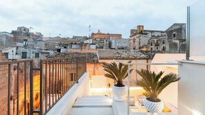 A rooftop terrace with a view of historic buildings, a railing, and potted plants.