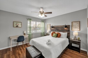 Ein Schlafzimmer mit einem Bett, einem Schreibtisch, einem Stuhl, einem Nachttisch und einem Deckenventilator.