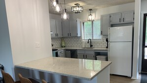 A kitchen with a central island, white cabinets, a refrigerator, and pendant lighting.