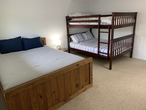 Un dormitorio con una cama grande de madera, una litera y una mesita de noche pequeña con una lámpara.