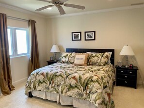 A bedroom with a bed, two nightstands, a ceiling fan, and a window with curtains.