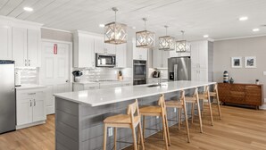 Una cocina moderna con armarios blancos, electrodomésticos de acero inoxidable, una isla grande con taburetes altos e iluminación colgante.