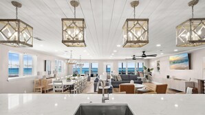 Amplia sala de estar con una isla grande en la cocina, mesa de comedor y zona de estar. Amplias ventanas ofrecen vistas al océano.