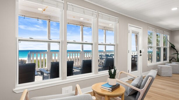 Una habitación con grandes ventanales con vista a una playa, amueblada con sillas y una mesa.