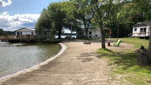 A lakeside property with a sandy beach, picnic tables, and a small dock. - Chickadee #3 Graceland Cottages (West Nipissing)