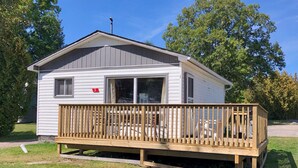 A small, single-story cabin with a wooden deck and a window. - Chickadee #3 Graceland Cottages (West Nipissing)