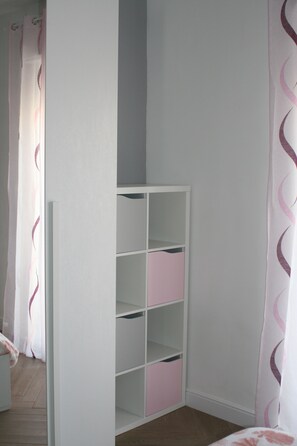 Ein Zimmer mit einem weißen Kleiderschrank, rosafarbenen Aufbewahrungsboxen und Holzboden.