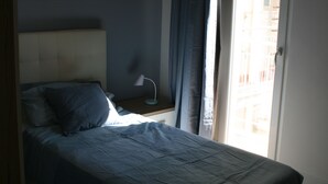 Quarto com cama, mesa de cabeceira, abajur e janela com cortinas.