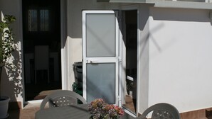 Pátio com mesa, cadeiras, planta em vaso e porta de vidro deslizante que dá para o interior.