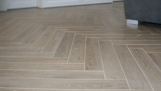 Quarto moderno com piso de madeira em padrão herringbone, armários brancos e sofá cinza estofado.