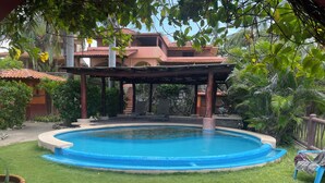 Une piscine entourée d’une terrasse, un espace de détente couvert et une végétation luxuriante.