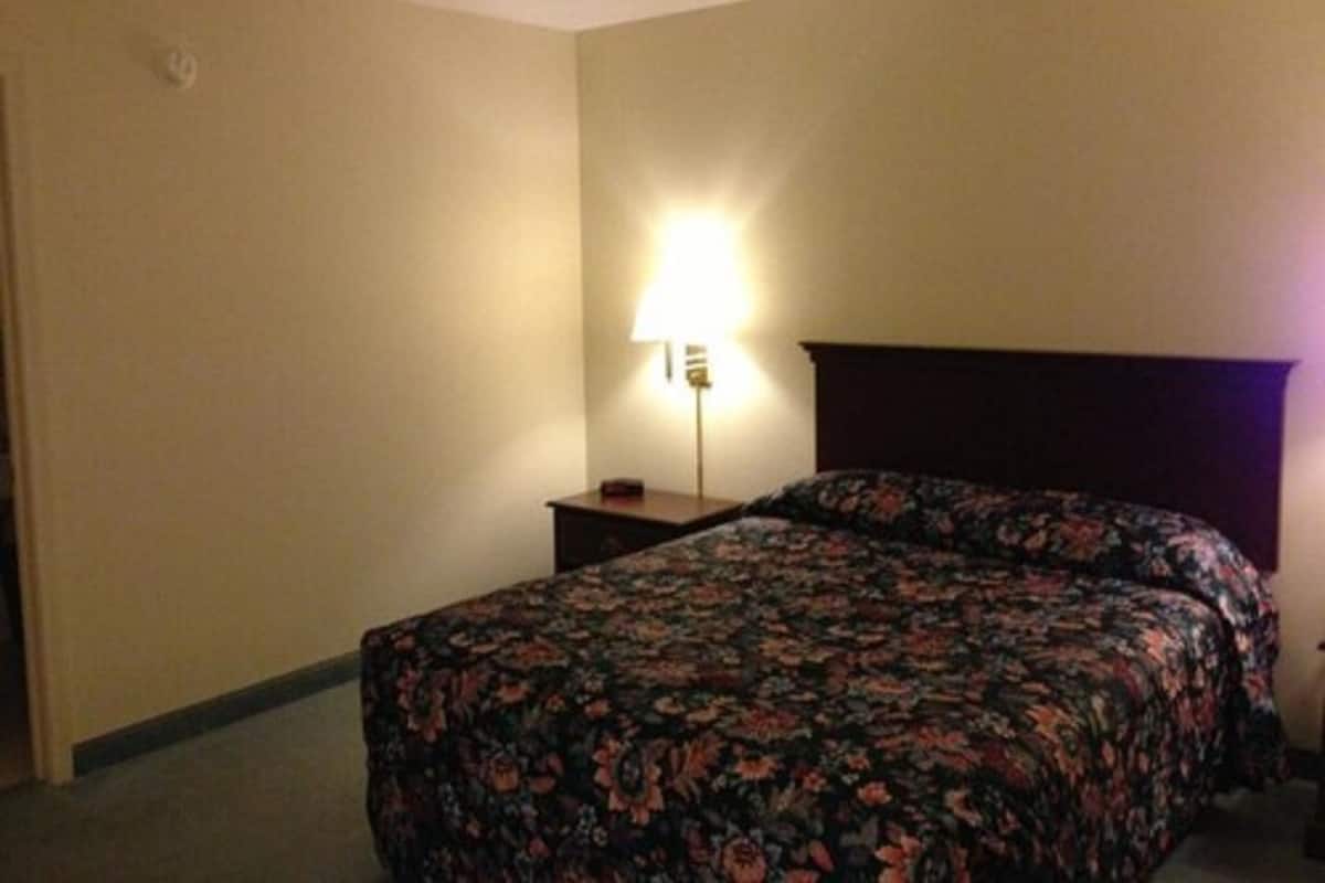 A hotel room with a bed, a nightstand, and a lamp.