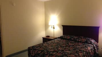 A hotel room with a bed, a nightstand, and a lamp.