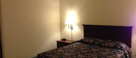 A hotel room with a bed, a nightstand, and a lamp.
