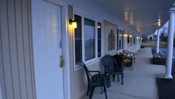 A covered porch with chairs and tables, a door, and windows with lights. - Gorgeous View Motel (Watkins Glen)